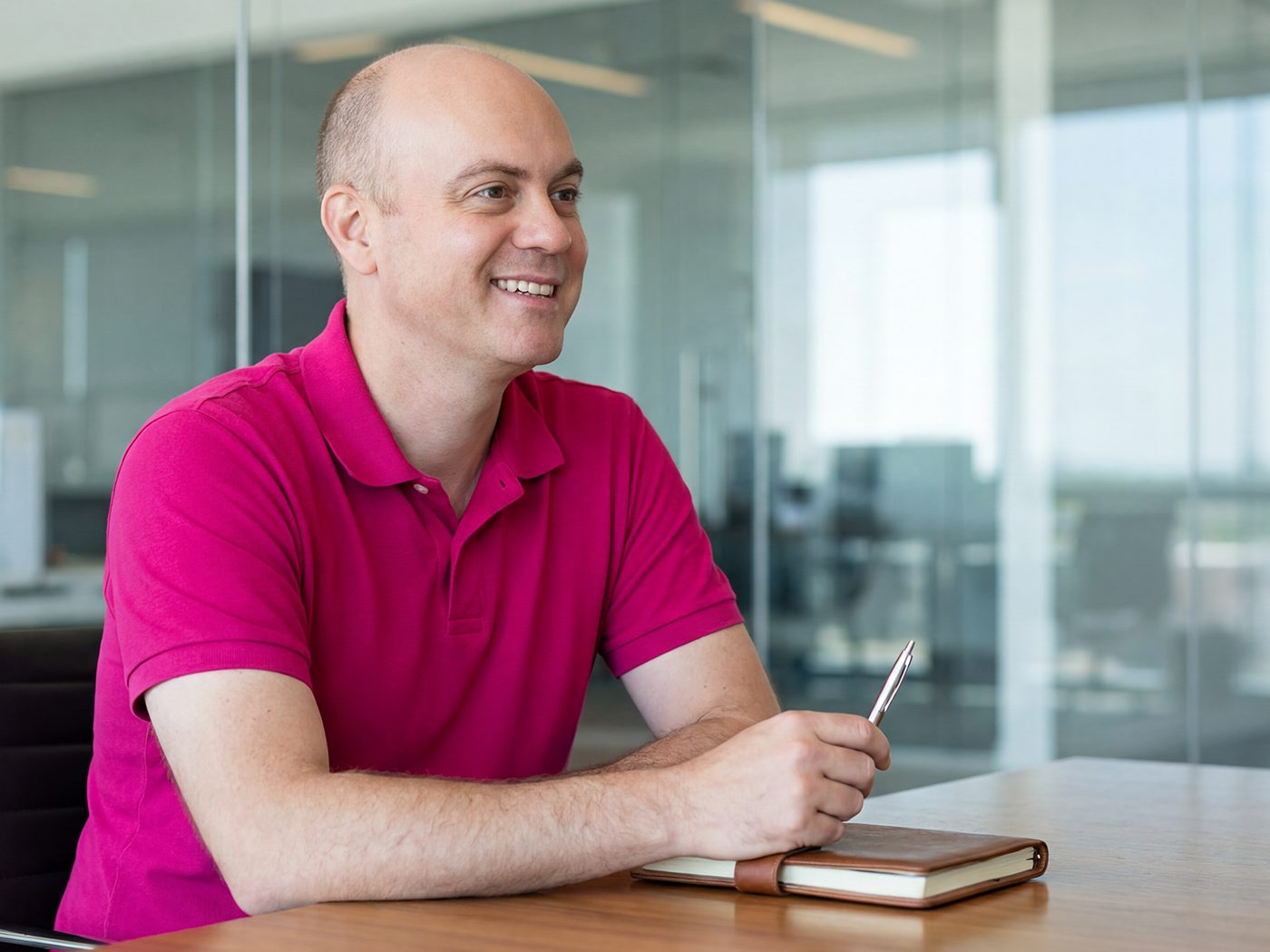 David Harbert at a boardroom table, in a fuchsia polo, mid-conversation